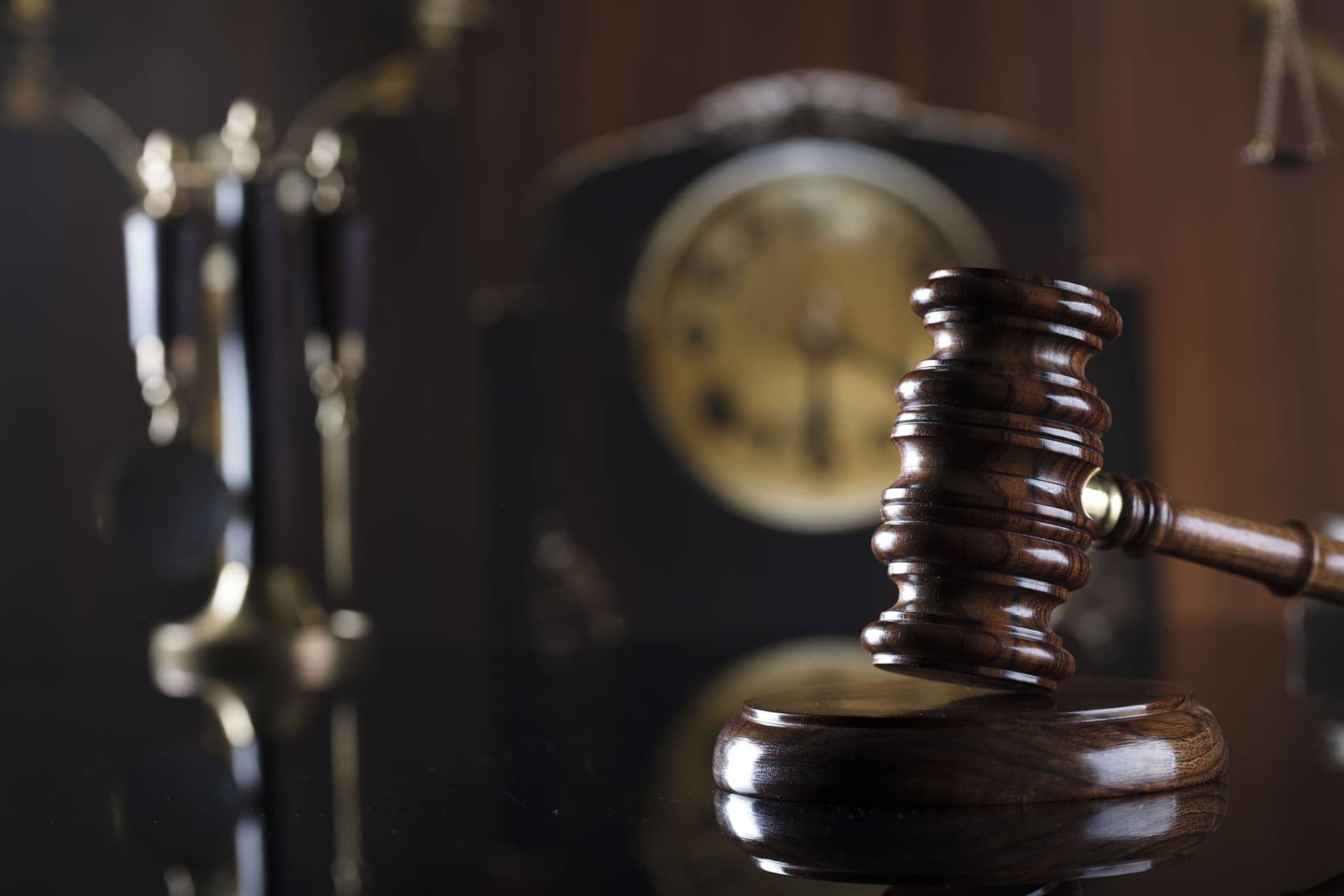 wooden judge's gavel on a reflective surface with a blurred clock in the background