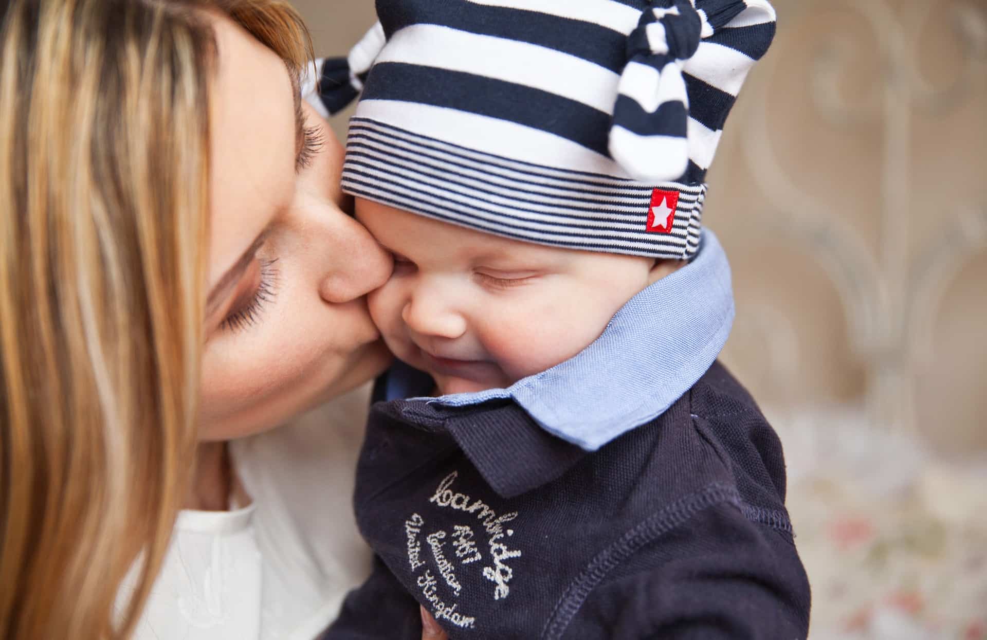 mother kissing her baby wearing a striped hat