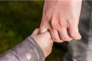 a child holding an adult's finger tightly with a close-up of their hands