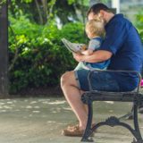 father sitting on a park bench with his young son while they deal with divorce