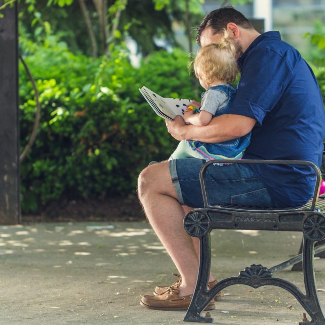 father sitting on a park bench with his young son while they deal with divorce