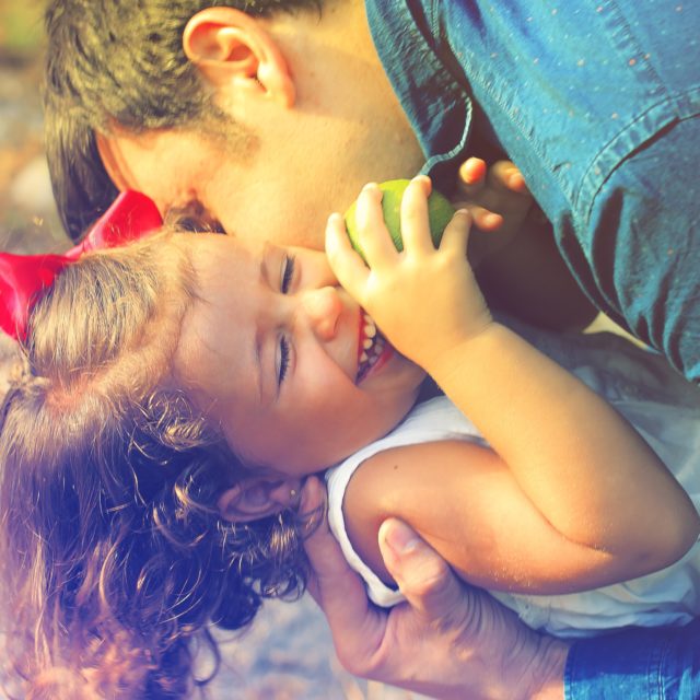Father holding and playing with his young daughter, both smiling