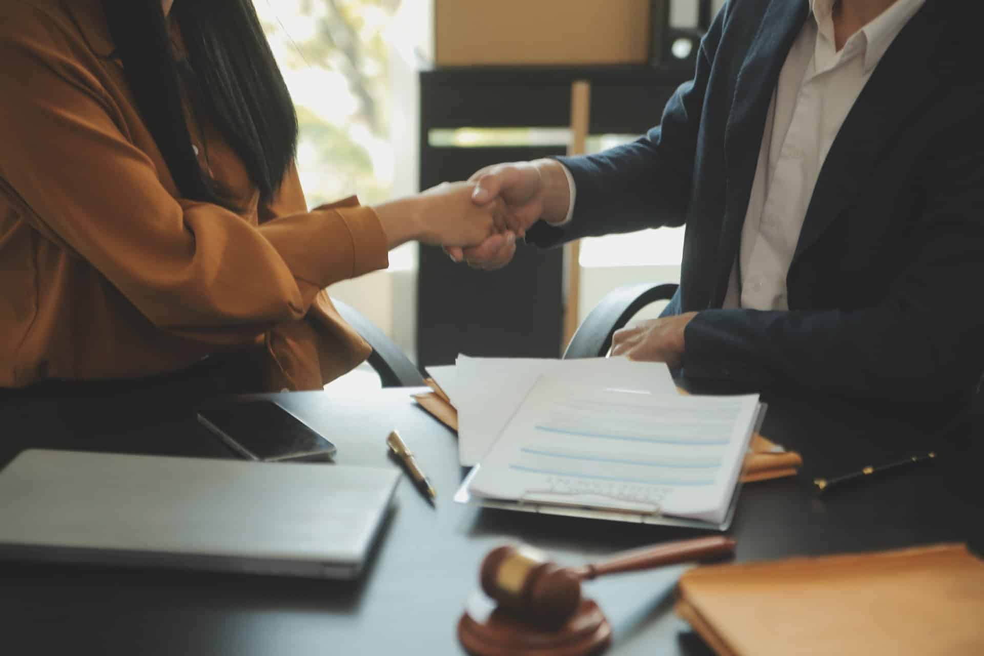 Professional handshake across a desk with documents and a gavel in view