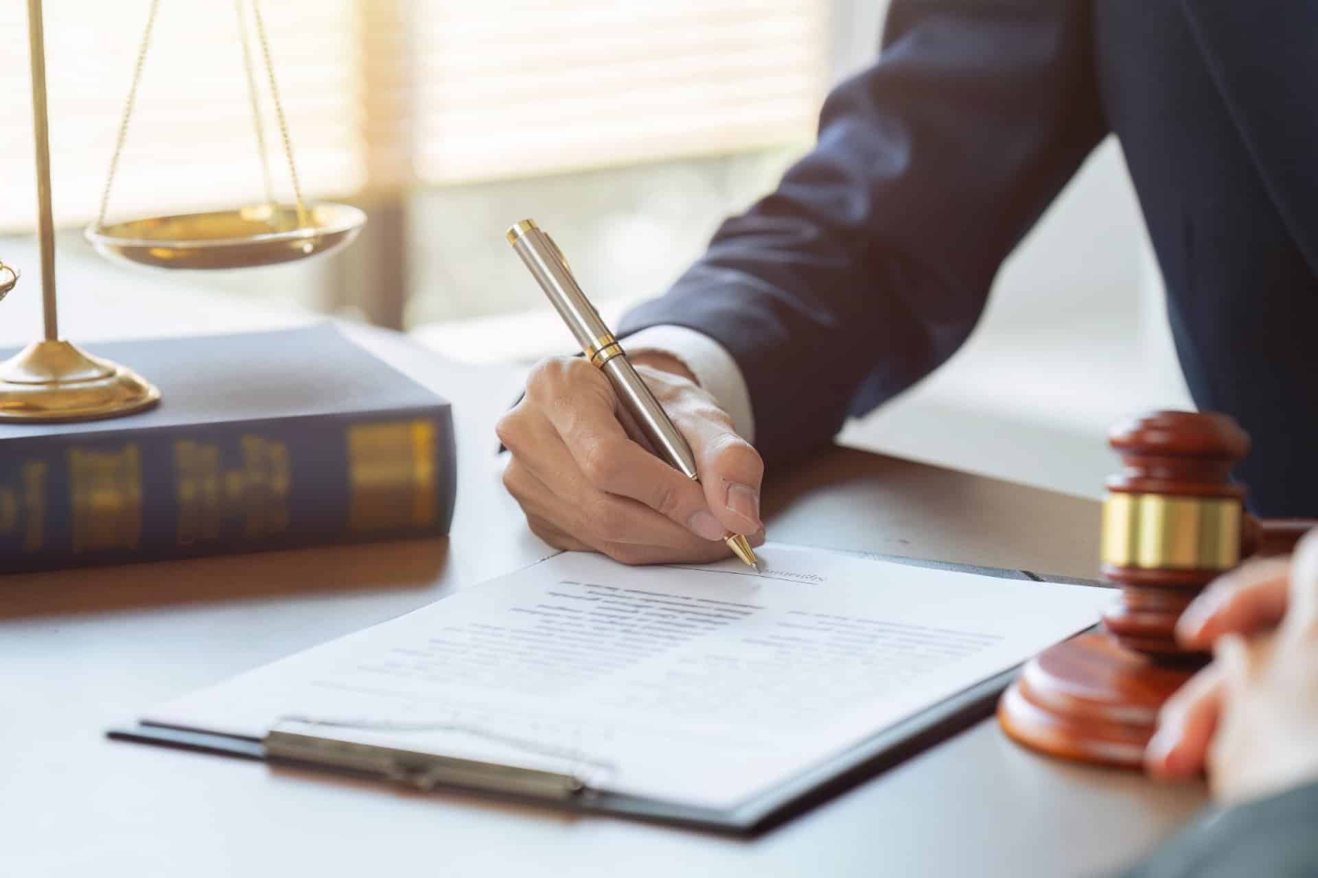 Lawyer signing legal documents at a desk with a gavel and scale in the background