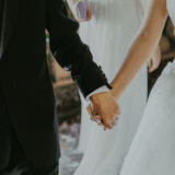 A bride and groom holding hands, showcasing their wedding attire as they walk together